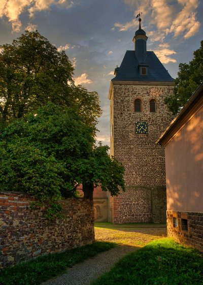 Das Foto zeigt einen Kirchturm, durch eine Häuserlücke fotografiert.