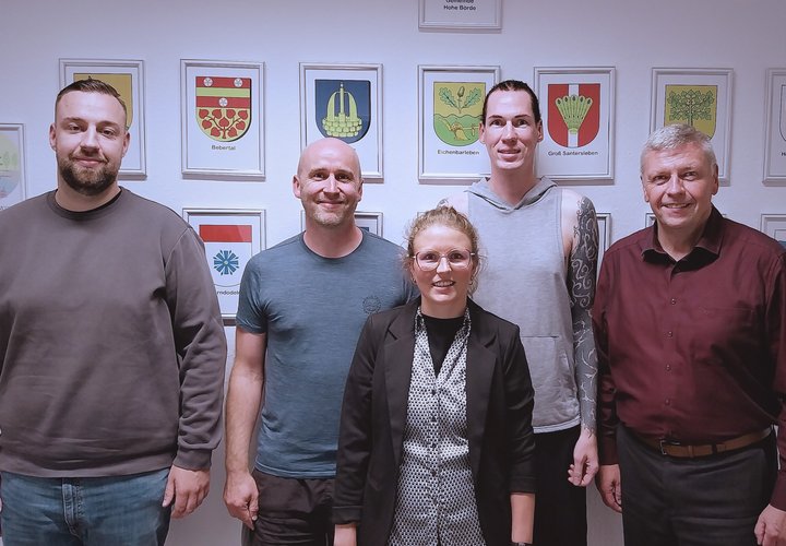 Das Bild zeigt vier Männer und eine Frau vor der Wappenwand im Rathaus der Gemeinde Hohe Börde