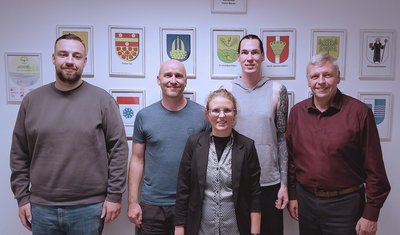 Das Bild zeigt vier Männer und eine Frau vor der Wappenwand im Rathaus der Gemeinde Hohe Börde