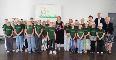 Mehrere Kinder in grünen T-Shirts, die Projektleiterin Marlies Böttcher, Bürgermeister Andreas Burger und die ehemalige Bürgermeisterin Steffi Trittel lächeln gemeinsam in die Kamera.