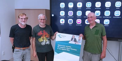 Dieses Foto zeigt drei Männer mit einem Plakat vor einem Smartboard.
