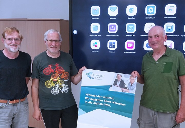 Dieses Foto zeigt drei Männer mit einem Plakat vor einem Smartboard.