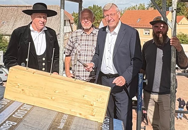 Vier Männer wollen beim Richtfest die Nägel einschlagen.
